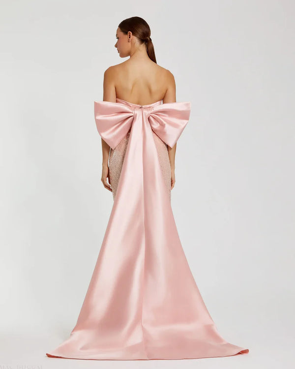 Model wearing Mac Duggal 37011 strapless gown featuring a sleek silhouette with an oversized bow detail on the back.  Back view.  Model wearing the color blush.