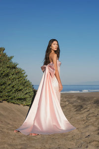 Model wearing Mac Duggal 37011 strapless gown featuring a sleek silhouette with an oversized bow detail on the back.  Back 3/4 view.  Model wearing the color blush.