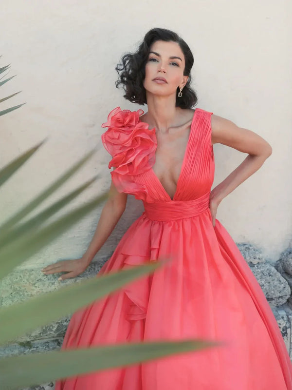 Model wearing Mac Duggal 48856 chiffon gown with V-neckline, ruffle shoulder detail, and flowing skirt.  Model wearing the color coral.  Front view.  Outdoors.