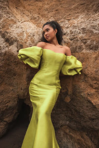 Model wearing Mac Duggal 50677 off-the-shoulder satin gown with puff sleeves, mermaid silhouette, and sweeping train.  Model is outdoors wearing the color chartreuse. Front view.