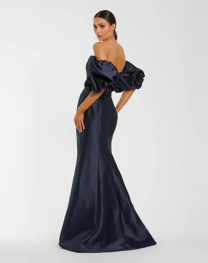 Model wearing Mac Duggal 50677 off-the-shoulder satin gown with puff sleeves, mermaid silhouette, and sweeping train.  Model is wearing the color midnight. 3/4 Front view.