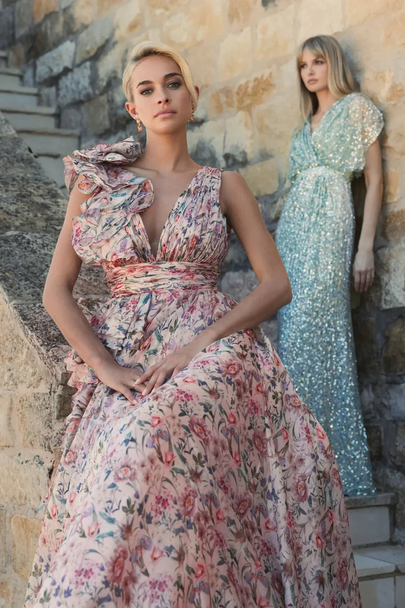 Model wearing Mac Duggal 68947 floral chiffon ballgown with plunging V-neckline, ruffle shoulder detail, and voluminous A-line skirt.  Model is wearing the dress in pinkMulti.  Front view.  Model in the back is wearing 5640 in seafoam.