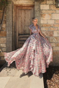 Model wearing Mac Duggal 68947 floral chiffon ballgown with plunging V-neckline, ruffle shoulder detail, and voluminous A-line skirt.  Model is wearing the dress in pinkMulti.  Front view.  Model is outside.