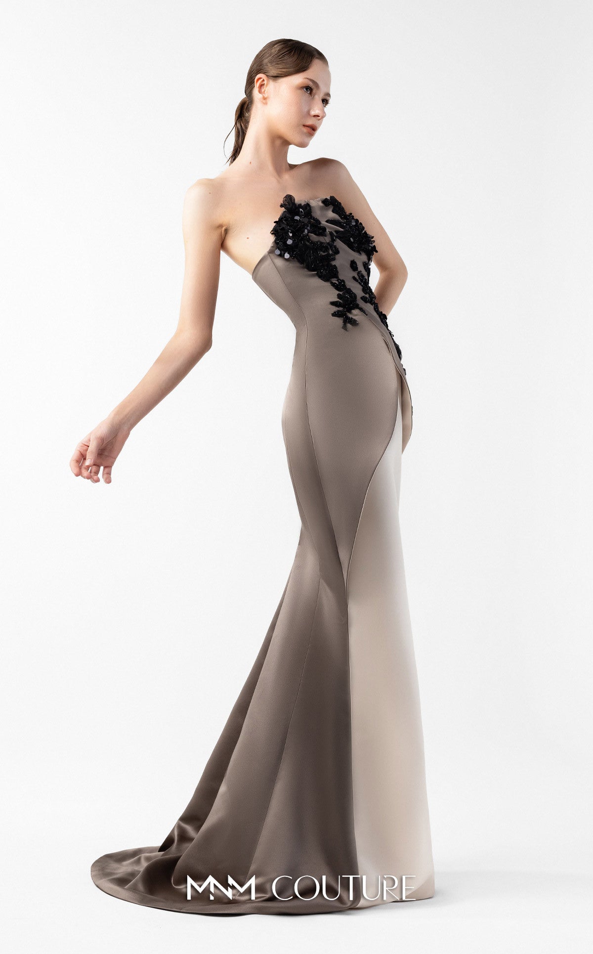 Model wearing the MNM Couture G2045 strapless sculpted evening gown featuring intricate bodice detailing and an asymmetrical floor-length silhouette.