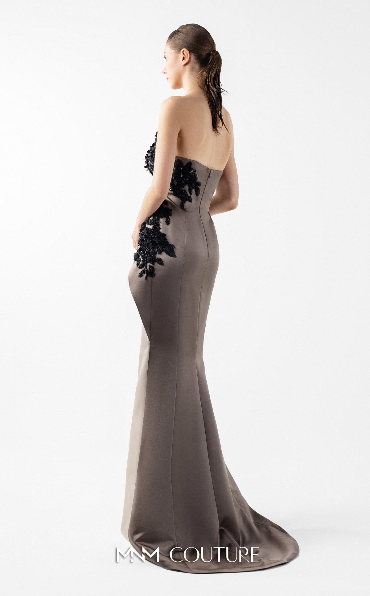 Model wearing the MNM Couture G2045 strapless sculpted evening gown featuring intricate bodice detailing and an asymmetrical floor-length silhouette.