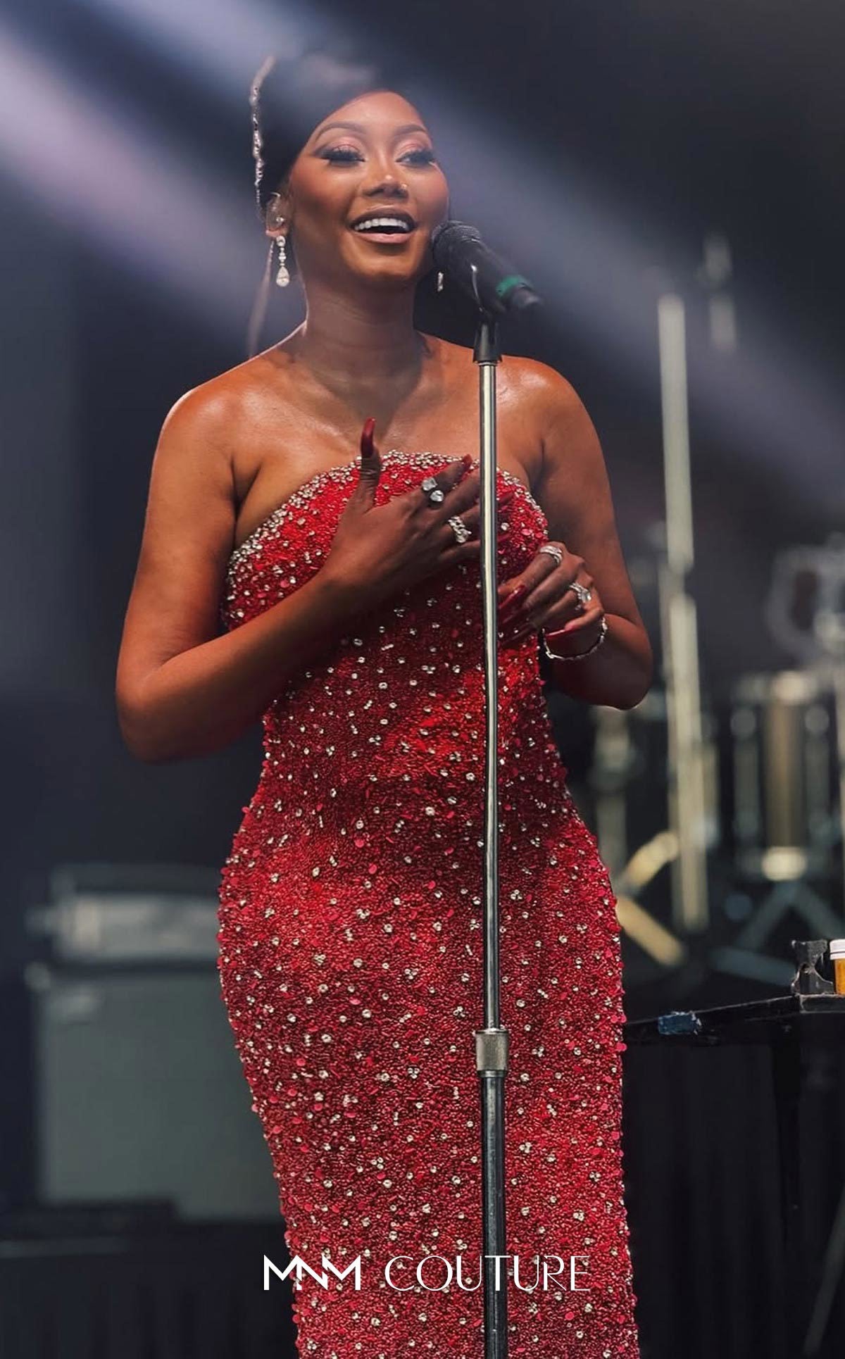 Woman in a red dress with sparkling details singing into a microphone on stage.