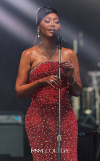 Woman in a red dress with embellishments singing into a microphone on stage.