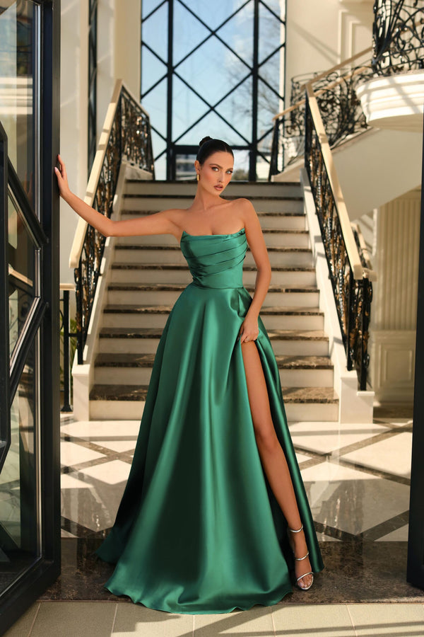 Model wearing Nicoletta NC1076 satin strapless gown with high slit in emerald green, showcasing ruched bodice and floor-length design.