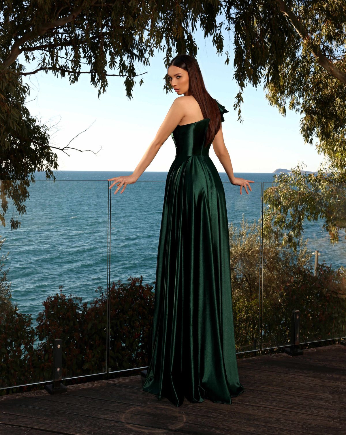 Model wearing Nicoletta NC2062 one-shoulder satin gown with ruffled shoulder and high slit in black, cadet blue, emerald, and vermillion.