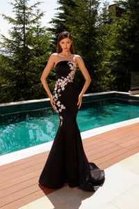 Model wearing Nicoletta NC2080 strapless black gown with blush floral embroidery in a mermaid silhouette by a pool.  Model is wearing the dress in the color black.
