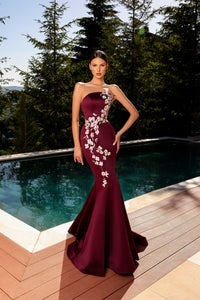 Model wearing Nicoletta NC2080 strapless black gown with blush floral embroidery in a mermaid silhouette by a pool.  Model is wearing the dress in the color burgundy.