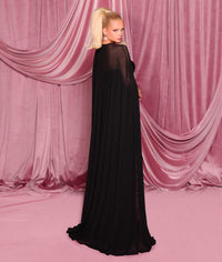 Model wearing Nicoletta NC3004 gown featuring a draped cape, strapless bodice, and front slit, posed against a pink curtain backdrop.