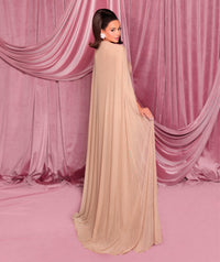 Model wearing Nicoletta NC3004 gown featuring a draped cape, strapless bodice, and front slit, posed against a pink curtain backdrop.