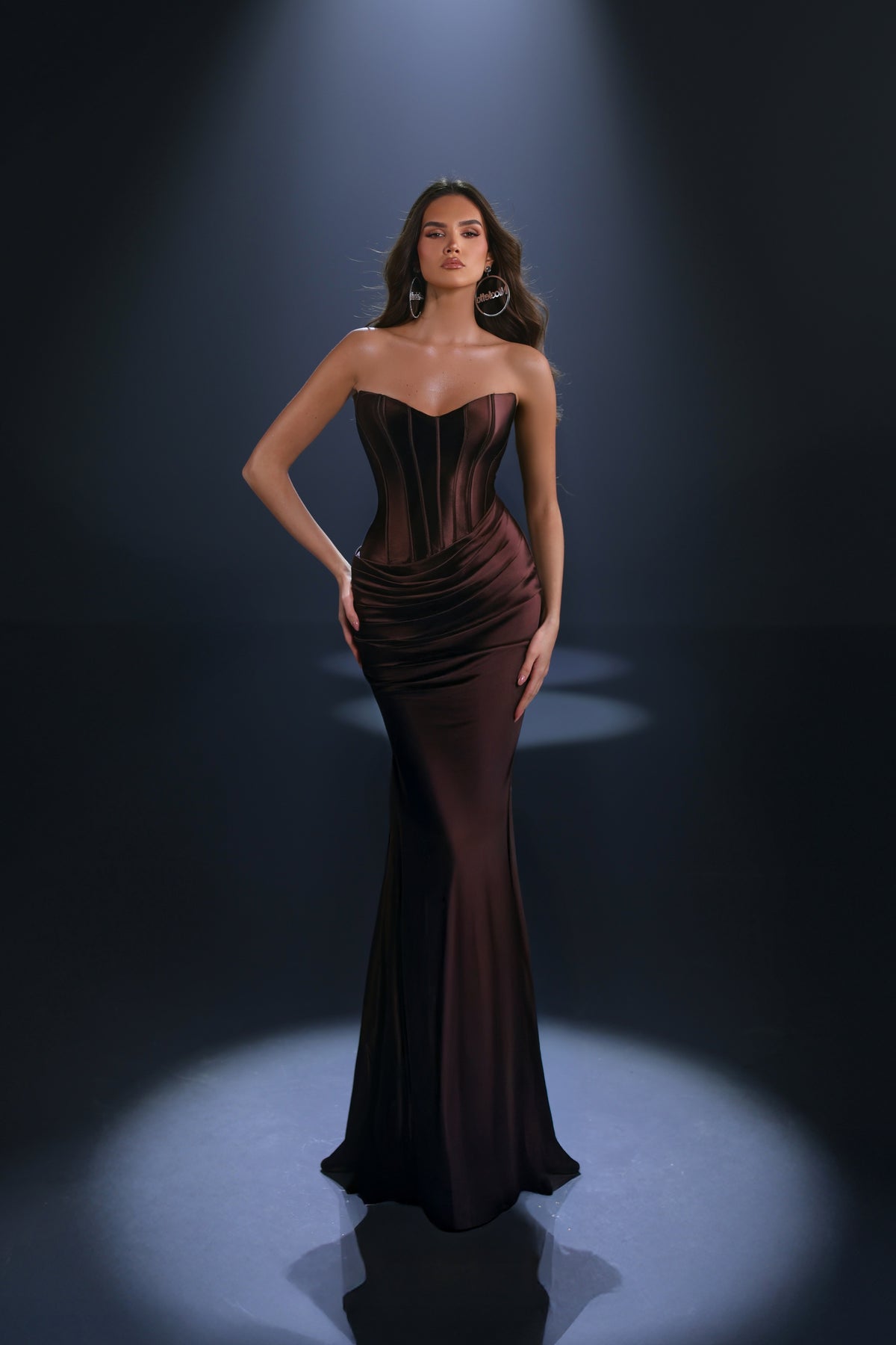 Woman wearing a dark brown strapless gown against a black background