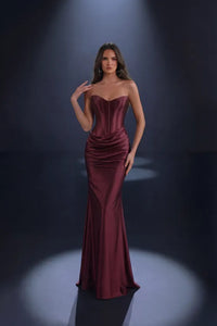 Woman wearing a mulberry color strapless gown against a dark background
