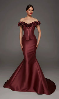 A woman modeling an off-the-shoulder mermaid gown in deep burgundy satin, featuring a structured corset-style bodice and a full flared skirt with a train, against a dark gray studio background.