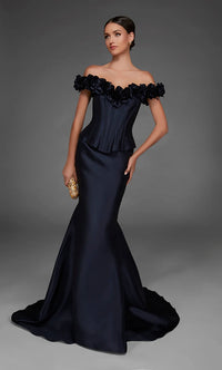 A woman models an off-the-shoulder navy blue mermaid gown with a ruffled peplum waist and a small gold clutch, set against a dark gray studio background.