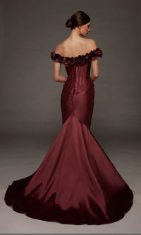 A woman modeling an off-the-shoulder mermaid gown in deep burgundy satin, photographed from the back against a dark gray studio backdrop.