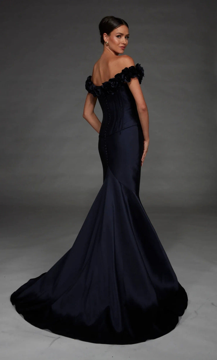 A woman modeling an off-the-shoulder mermaid gown in dark navy satin, photographed against a dark gray studio backdrop.