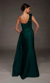 A woman modeling a floor-length one-shoulder evening gown from the back, shown against a dark gray studio background. The dress is a rich emerald green satin with a structured one-shoulder neckline, ruffled detailing, and a draped skirt.