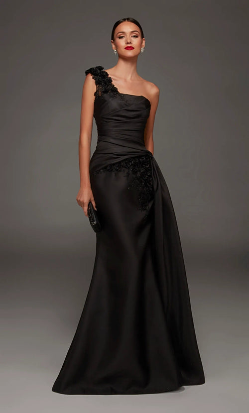 A woman modeling a floor-length black one-shoulder evening gown with a draped satin skirt and floral lace applique details, posed against a dark gray studio background.