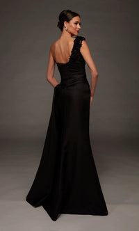 A woman modeling a floor-length black evening gown from the back, featuring a one-shoulder design with ruffled detailing on the shoulder and a structured back, set against a dark gray studio background.