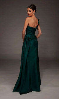 A woman modeling a floor-length dark green satin gown from the back, featuring a one-shoulder strap design and a draped waist, set against a dark gray studio background.
