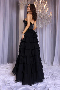 Model wearing Portia & Scarlett PS25961 gown featuring a strapless embellished bodice, sheer corset, high slit, and tiered ruffle skirt.