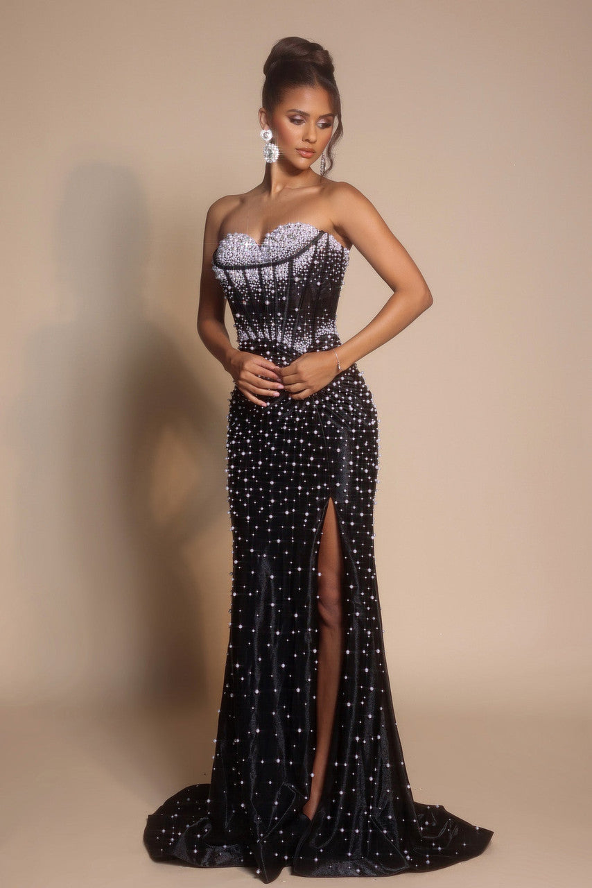 Woman wearing a black strapless evening gown with a high slit on a beige background