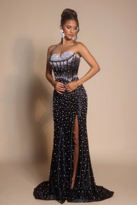 Woman wearing a black strapless evening gown with a high slit on a beige background