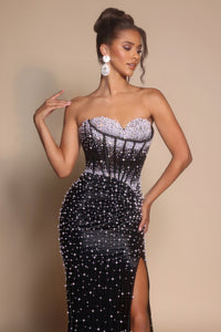 Woman wearing a black strapless gown with silver embellishments against a beige background