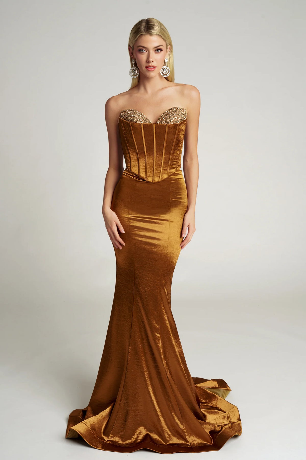 Woman wearing a gold evening gown with a fitted bodice and long train on a white background