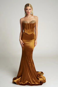 Woman wearing a gold evening gown with a fitted bodice and long train on a white background