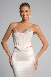 Woman wearing a strapless white gown with embellishments on a gray background