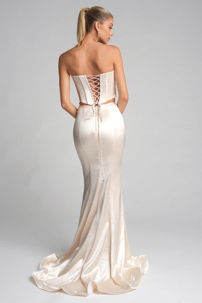 Woman wearing a strapless, backless white evening gown with a lace-up detail on a gray background