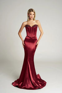 Woman wearing a strapless burgundy evening gown on a plain background