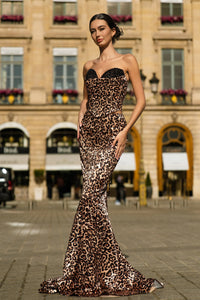 Woman in a leopard print evening gown standing in an urban setting.