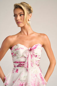 Woman wearing a strapless floral dress with pink and white flowers on a plain background