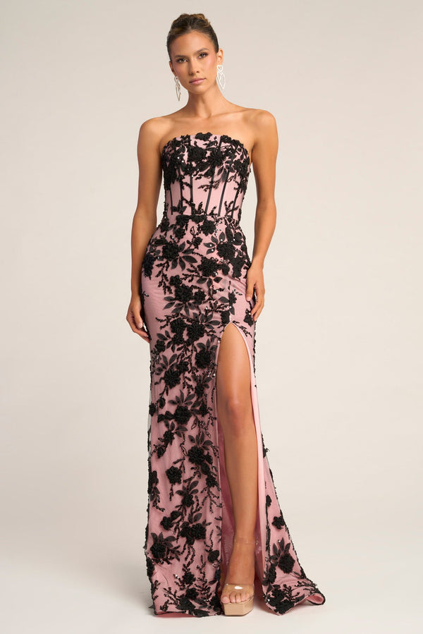 Woman wearing a strapless floral evening gown with a high slit on a plain background