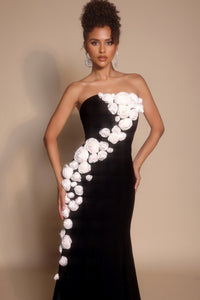 Woman wearing a black strapless gown with white floral embellishments against a beige background