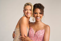 Two women in glamorous dresses posing against a plain background