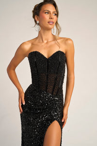 Woman wearing a black beaded dress with a slit on a plain background