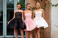 Three women wearing black, pink, and white dresses standing outdoors.