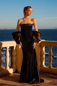 Woman in a black strapless gown with puffed sleeves standing on a balcony overlooking the ocean.