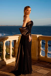 Woman in a black evening gown standing on a balcony overlooking the ocean.