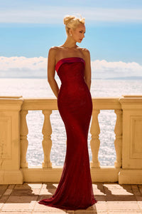 Woman in a red evening gown standing on a balcony with ocean view