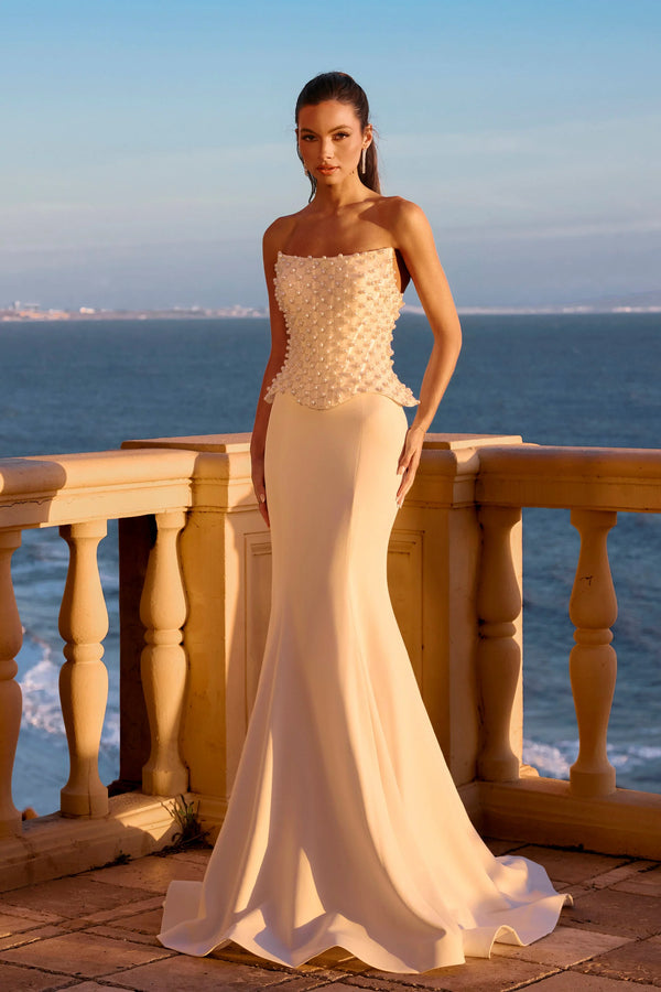 Woman in a strapless beige evening gown standing on a balcony with ocean view