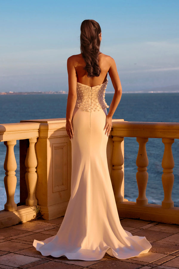 Woman in a white evening gown standing on a balcony overlooking the ocean.