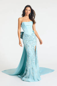 A woman modeling a strapless light blue evening gown with a fitted corset-style bodice, heavily embroidered floral detailing, a thigh-high slit, and a long flowing train against a plain light gray studio background.