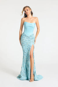 A woman modeling a strapless light blue gown with a fitted corset-style bodice, floral lace overlay, and a high front slit, photographed against a plain light gray studio background.